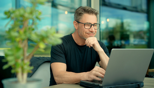 Smilende mand sidder ved bord og kigger på sin computer